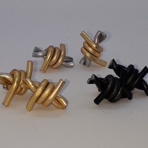 May include: Four small barbed wire earrings in silver, gold, and black. The earrings are made of metal and are shaped like barbed wire.