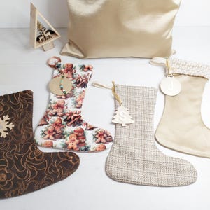 May include: A selection of Christmas stockings in different styles. One is brown with a snowflake, another has a gingerbread man pattern, and a third is a neutral woven fabric. Each stocking has a hanging loop and decorative tags.