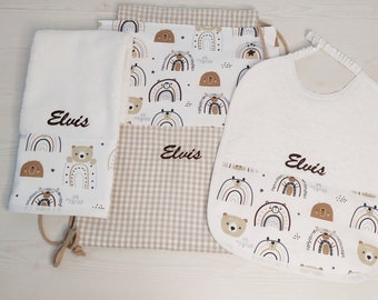 May include: A set of baby items with a rainbow and bear design. The set includes a bib, a towel, and a drawstring bag. All items are white with brown and beige accents and feature the name "Elvis" embroidered on them.