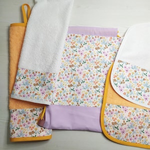 Può includere: Un set di asciugamani e lavette con motivo floreale. Gli asciugamani sono arancioni e bianchi, con un bordo floreale dai colori pastello. Le lavette hanno un design simile, con un accento lavanda. Realizzato in materiale morbido.