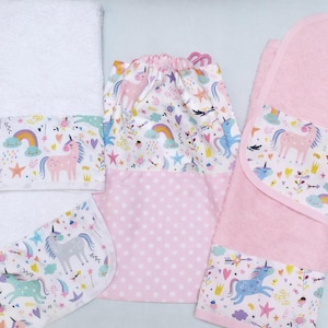 Puede incluir: Un conjunto de artículos para bebés con motivos de unicornios. El conjunto incluye dos baberos, una toalla y una bolsa con cordón. Los artículos son blancos y rosas, con un colorido estampado de unicornios, arcoíris y estrellas.