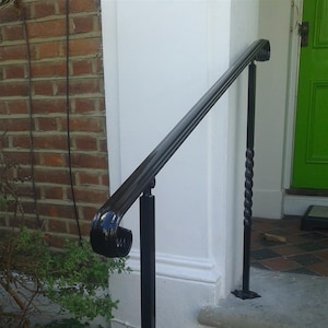May include: Black metal handrail with a twisted base and a decorative scroll at the top. The handrail is mounted to a white wall and a brick wall.