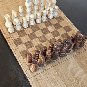 May include: A wooden chess set with light and dark pieces arranged on a checkered board. The light pieces are ivory-colored, while the dark pieces are brown. The board is made of light-colored wood with a grid of squares.