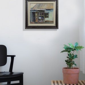 May include: A framed painting of a small, green building with a brown roof. The building has a door and a window. The painting is in a dark brown frame with a decorative border.