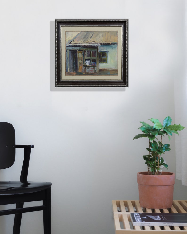 May include: A framed painting of a small, green building with a brown roof. The building has a door and a window. The painting is in a dark brown frame with a decorative border.