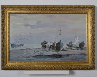 Op de afbeelding: Een ingelijst olieverfschilderij dat een zeezicht met drie boten op een zandstrand afbeeldt. De boten zijn verweerd en hebben zeilen en masten. De lucht is lichtblauw met witte wolken. Het schilderij is in een gouden lijst.