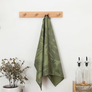 May include: A wooden wall-mounted hook rack with five hooks, a green patterned kitchen towel hanging from one of the hooks, a potted plant, and a wooden spice rack with glass bottles and jars.
