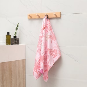 May include: A wooden wall-mounted hook rack with four hooks. A pink floral patterned towel is hanging on one of the hooks.