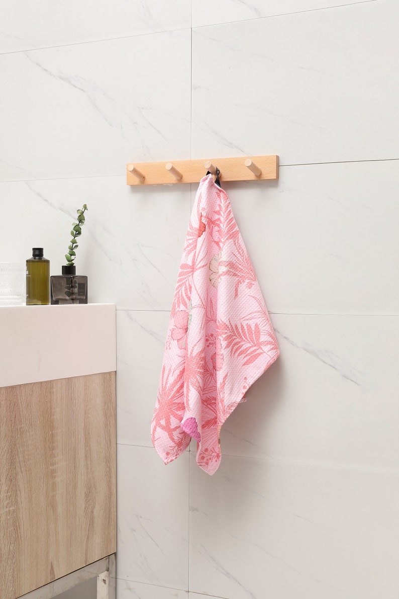 May include: A wooden wall-mounted hook rack with four hooks. A pink floral patterned towel is hanging on one of the hooks.