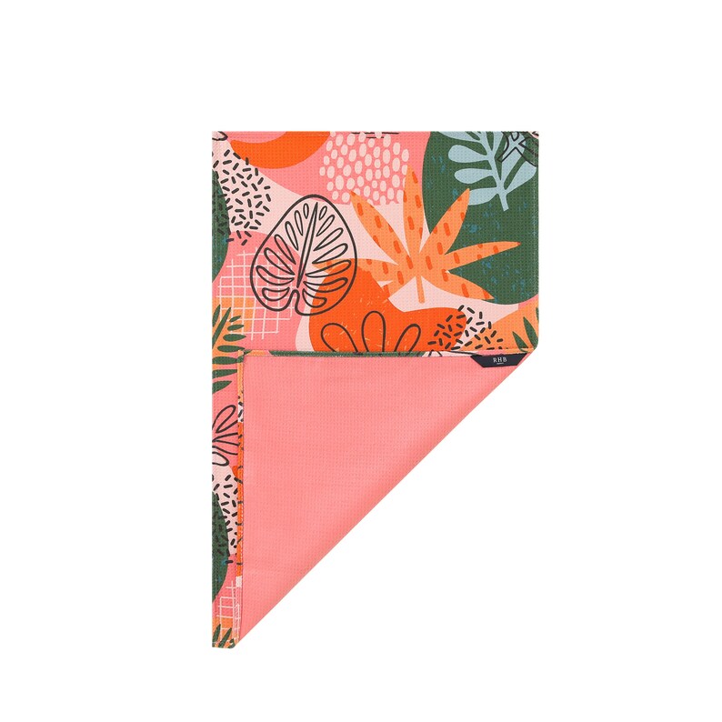 K&ouml;nnte beinhalten: Eine gefaltete Yogamatte mit einem lebendigen tropischen Bl&auml;ttermuster in Koralle, Orange, Gr&uuml;n und Schwarz. Die Unterseite ist einfarbig korallenfarben. Das Design umfasst gro&szlig;e stilisierte Bl&auml;tter und abstrakte Formen.