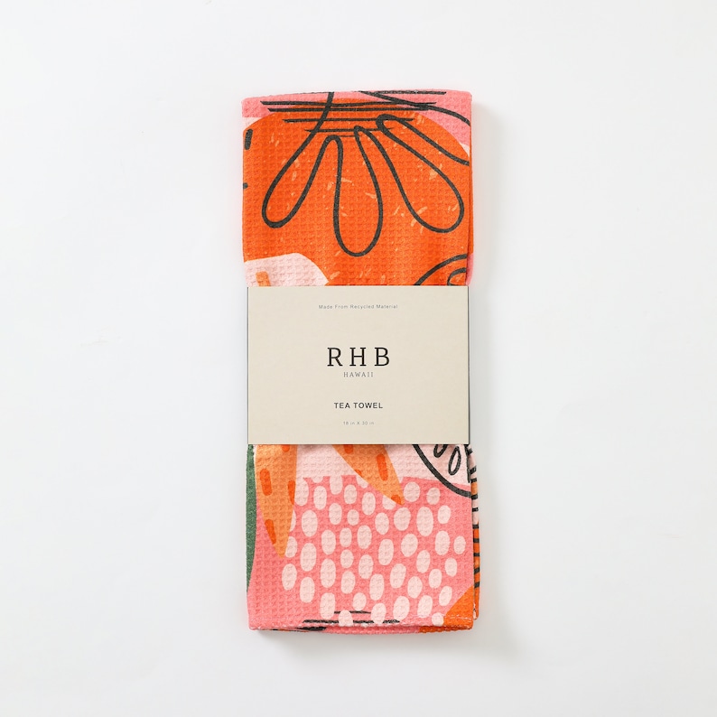K&ouml;nnte beinhalten: Ein gefaltetes Geschirrtuch mit einem farbenfrohen, abstrakten Blumendesign. Das Tuch ist orange, rosa und gr&uuml;n mit schwarzen Umrissen. Das Etikett lautet "RHB HAWAII TEA TOWEL" und das Tuch misst 45,7 x 76,2 cm.
