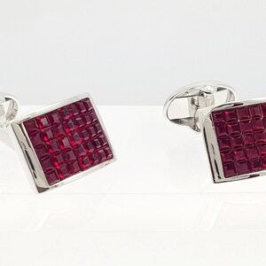 May include: A pair of silver cufflinks with square red crystal accents.