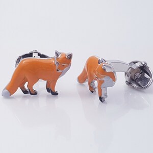 May include: A pair of silver cufflinks featuring a fox design. The foxes are orange with black eyes and noses. The cufflinks are a great way to add a touch of whimsy to any outfit.