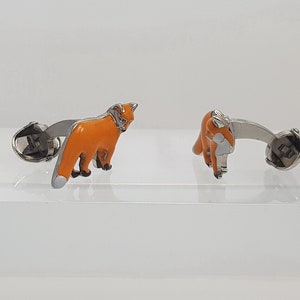 May include: A pair of silver cufflinks with orange enamel fox designs. The foxes are facing different directions.