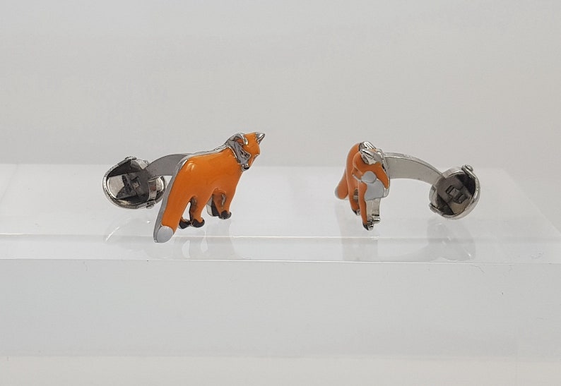 May include: A pair of silver cufflinks with orange enamel fox designs. The foxes are facing different directions.