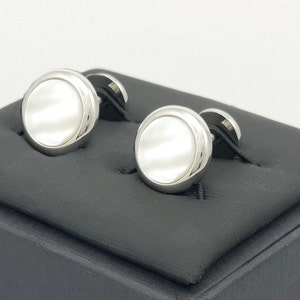 May include: A pair of silver cufflinks with white mother-of-pearl insets. The cufflinks are displayed on a black velvet box.