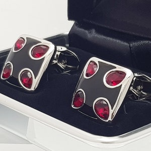 May include: A pair of cufflinks with a black enamel finish and four red gemstones. The cufflinks are in a black velvet box.