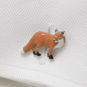 May include: Silver cufflinks with an orange fox design. The fox is standing on all four legs with its tail curled behind it.