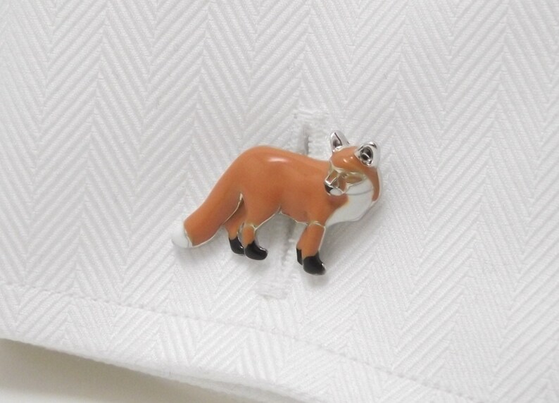 May include: Silver cufflinks with an orange fox design. The fox is standing on all four legs with its tail curled behind it.