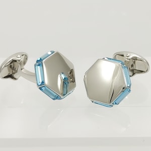 May include: A pair of silver cufflinks with a hexagonal blue crystal design.