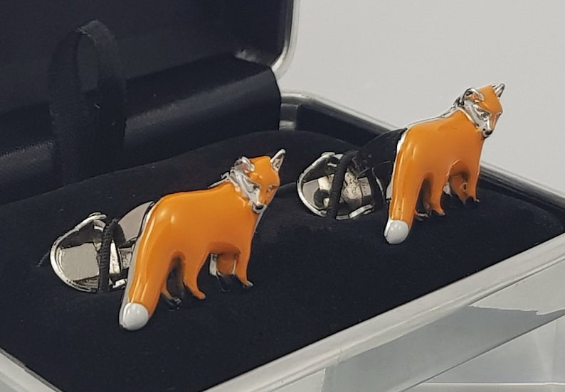 May include: A pair of silver cufflinks with orange enamel fox designs. The cufflinks are in a black velvet box.