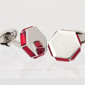 May include: A pair of silver cufflinks with red geometric designs. The cufflinks are hexagonal in shape and have a polished silver finish.