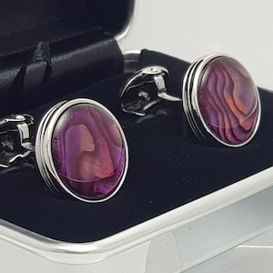 May include: A pair of silver cufflinks with a round, iridescent purple and pink abalone shell inlay. The cufflinks are in a black velvet box.