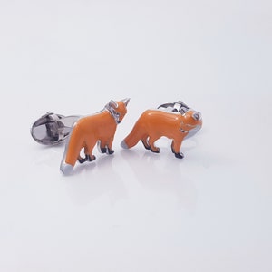 May include: A pair of silver fox cufflinks with orange enamel. The foxes are facing forward with their tails curled behind them.