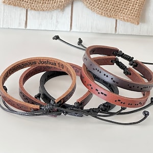 May include: Four leather bracelets with different engravings. One bracelet has the text "Be Strong and Courageous Joshua 1:9", another has the text "Always find you", another has the text "Love to", and the last bracelet has braille text.