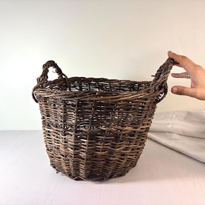May include: A round, dark brown woven basket made of natural twigs or branches. The basket features a deep, open-top design with two sturdy, integrated handles on opposite sides, showcasing a rustic, textured, and hand-woven construction.
