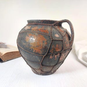 Könnte beinhalten: Eine weiße Keramik-Tasse mit schwarzem Henkel und dem Text "But First, Coffee" in schwarzer, handschriftlicher Schrift. Die Tasse steht auf einer weißen Oberfläche.
