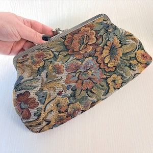 Op de afbeelding: Een rechthoekige clutch van geweven tapijtstof met een veelkleurig bloemenpatroon in tinten oranje, geel, groen en blauw. De tas heeft een zilverkleurig metalen frame met een knipsluiting aan de bovenkant in het midden.