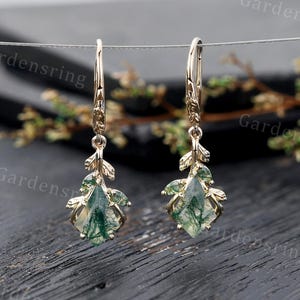 May include: Gold dangle earrings with green moss agate gemstones and leaf accents.
