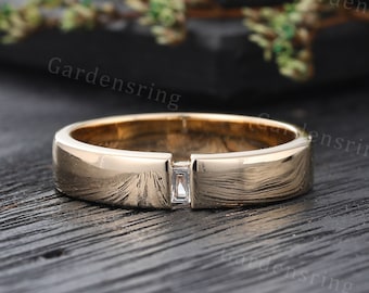 May include: A gold band with a single, rectangular, clear gemstone set in the center.