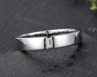 Op de afbeelding: Een zilveren bandring met een enkele, kleine, rechthoekige diamant in het midden.