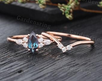May include: A rose gold engagement ring set with a marquise cut blue gemstone surrounded by smaller round diamonds. The matching wedding band is a delicate v-shaped band with round diamonds.