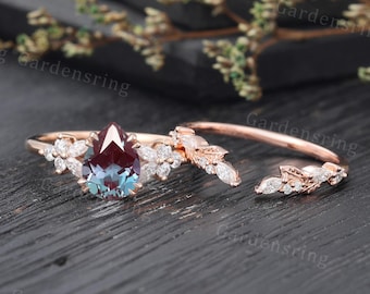 May include: A pear-shaped alexandrite engagement ring set in rose gold with a delicate floral design and a matching band. The alexandrite is surrounded by smaller diamonds.