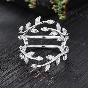 Può includere: Un anello d'argento con un delicato design di foglie e piccoli diamanti. L'anello è diviso in due parti, con le foglie che formano un motivo continuo.