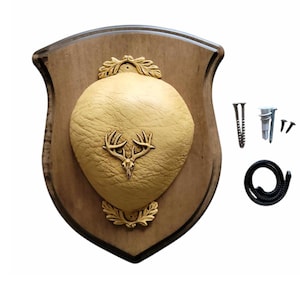 May include: A wooden plaque with a gold-coloured deer head silhouette and a gold-coloured oval plaque. The plaque is mounted on a brown wooden shield shape. The plaque comes with mounting hardware, including screws and a hanging cord.