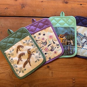 May include: Six rectangular quilted pot holders arranged in a fan shape. Each features a unique graphic print including foxes, birds, a bear, orcas, fish, and abstract geometric patterns in black, red, white, blue, purple, and green.
