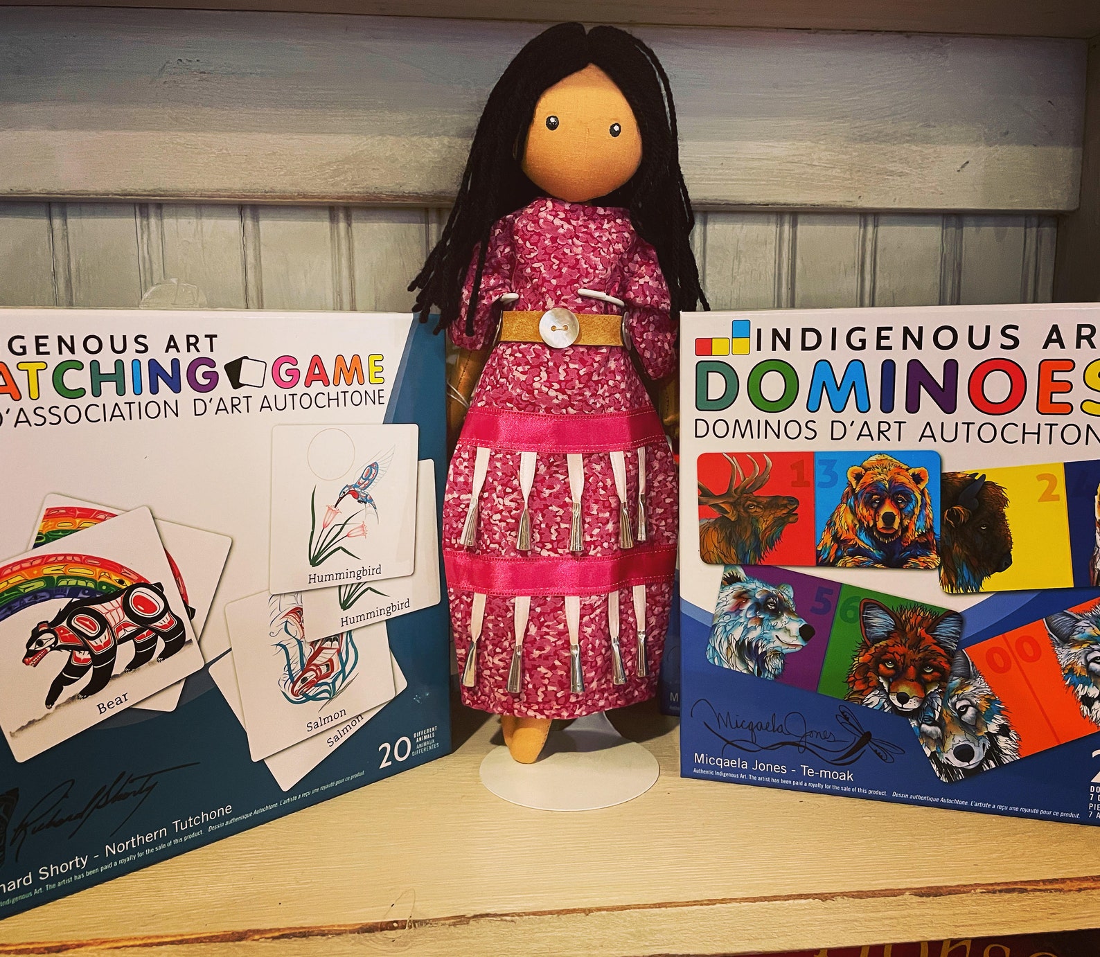 Two Indigenous children's games with an Indigenous doll in between them.