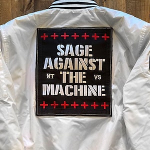 May include: White bomber jacket with a black and red embroidered patch that says "Sage Against The Machine" with the words "NT" and "VS" on either side of "The".