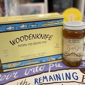 May include: A yellow rectangular box of Woodenknife Indian Fry Bread Mix with a net weight of 680 grams, alongside a glass jar of Big Sky Honey, raw unfiltered high mountain clover honey with a net weight of 297 grams, featuring white lids.