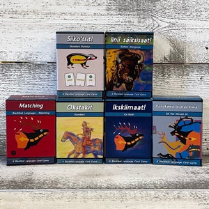 May include: Six Blackfeet Language card games with colorful illustrations. The games include: Matching, Okstakít Numbers, Ikskiimaat! Go Hunt, Ponokawa Ipsstáo'kiwa! Elk Has Moved In!, Siiko'tsit! Numbers Rummy, and liníí sáíksisaat! Buffalo Stampede.