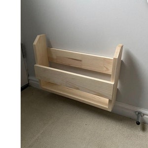 Könnte beinhalten: Ein Wandregal aus Naturholz mit zwei Ablagen. Das Regal ist an einer weißen Wand montiert und hat ein schlichtes Design.