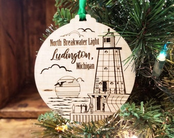 May include: A wooden Christmas ornament featuring a black and white illustration of the North Breakwater Light in Ludington, Michigan. The ornament is round and has a green ribbon attached.