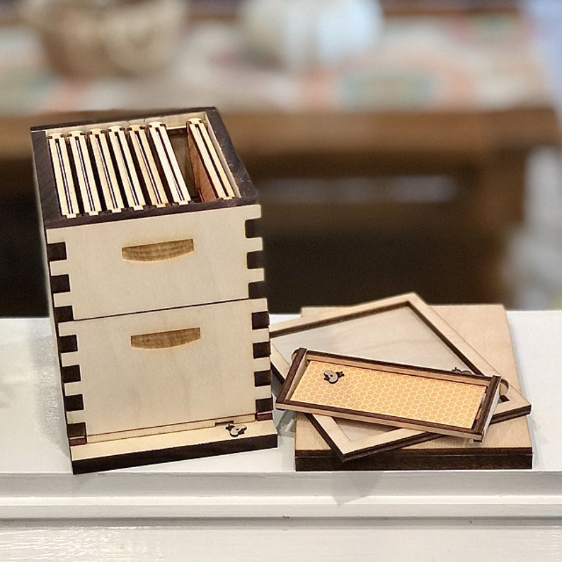 Puede incluir: Una caja de madera con dos cajones y una tapa extra&iacute;ble. La caja est&aacute; hecha de madera clara con molduras de color marr&oacute;n oscuro. La tapa de la caja tiene un patr&oacute;n de panal.