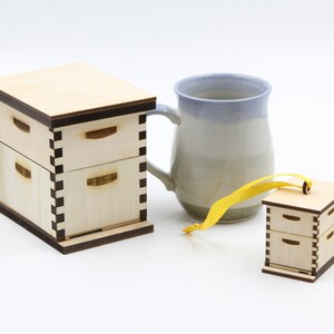 May include: Two wooden boxes with a honeycomb design, one is a small ornament with a yellow ribbon, the other is larger and has a ceramic mug next to it.