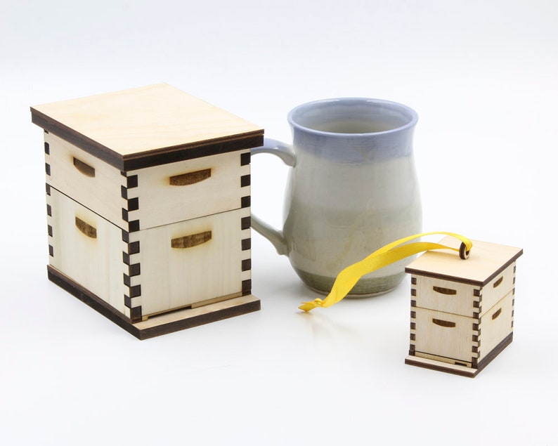 May include: Two wooden boxes with a honeycomb design, one is a small ornament with a yellow ribbon, the other is larger and has a ceramic mug next to it.