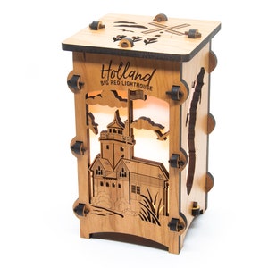 Puede incluir: L&aacute;mpara de madera con un dise&ntilde;o recortado del Big Red Lighthouse en Holland, Michigan. La l&aacute;mpara est&aacute; iluminada desde el interior, creando un brillo c&aacute;lido. El texto "Holland Big Red Lighthouse" est&aacute; grabado en la parte delantera de la l&aacute;mpara.